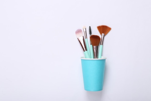 Makeup brushes in cardboard cup on white background