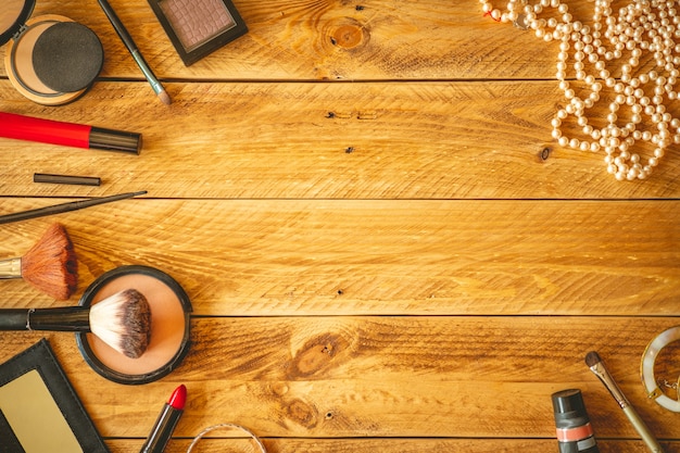 Makeup products and jewelry on a wooden table with copy space.