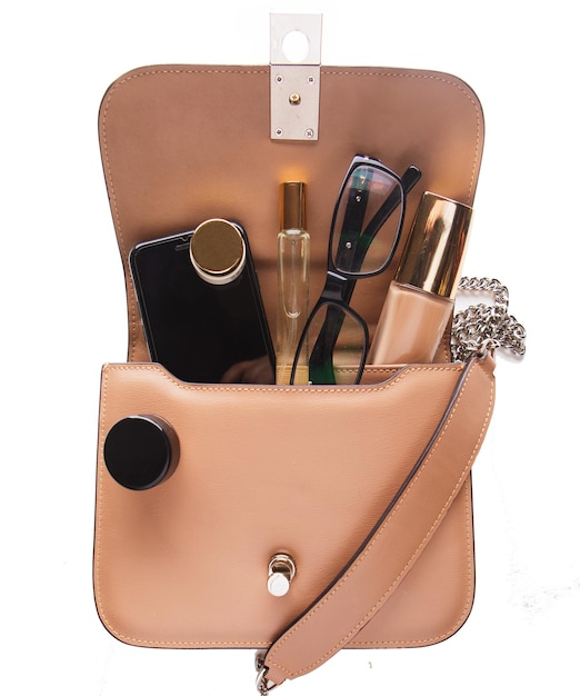 Makeup products and mobile in trendy handbag on white background Close up