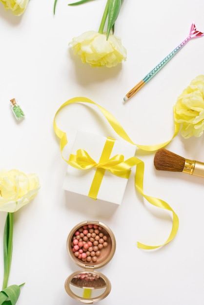 Makeup products with yellow tulip flowers and a gift box with a bow on a white background