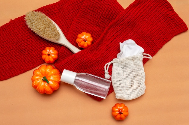 Makeup remover, brush and natural reusable sponges in a bag on a beige background with a red scarf and orange pumpkins. Autumn layout. Top view, flatly