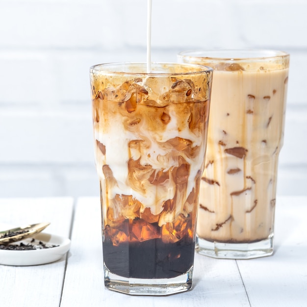 Making bubble tea, pouring blend milk tea into brown sugar pattern drinking glass cup on white wooden table background, close up, copy space