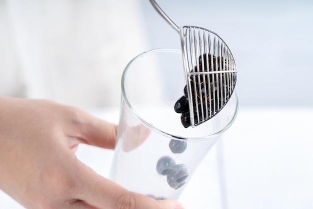 Making bubble tea scoop and pour cooked brown sugar flavor tapioca pearl bubble balls into cup on white wooden table background close up copy space