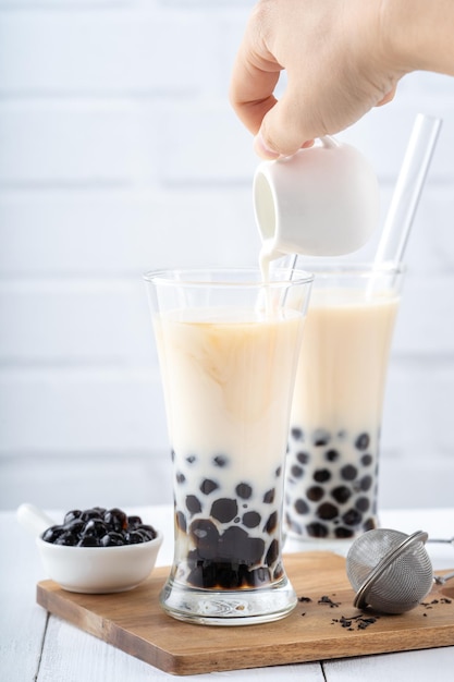 Making bubble tea scoop and pour cooked brown sugar flavor tapioca pearl bubble balls into cup on white wooden table background close up copy space