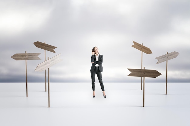 Making business decision and questions dilemma concept with pensive young businesswoman surrounded by wooden arrow sign boards choosing direction