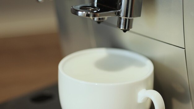 Making cappuccino using automatic coffee machine Coffee is pouring into cup with frothed milk or cream closeup Beverage drink for breakfast