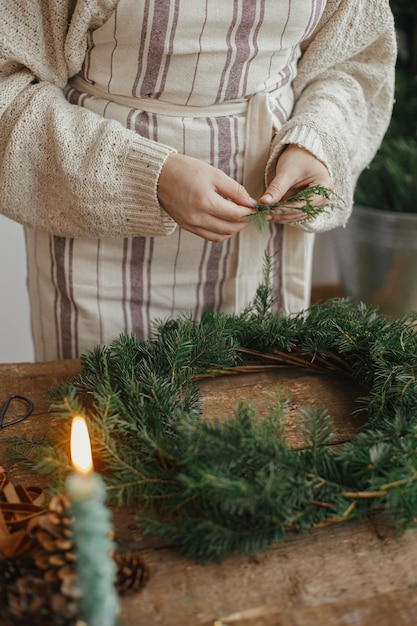 Making Christmas rustic wreath Woman hands holding cedar branches and making wreath on wooden table