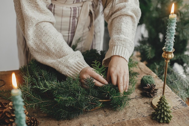 Making Christmas rustic wreath Woman hands holding fir branches and making wreath on wooden table