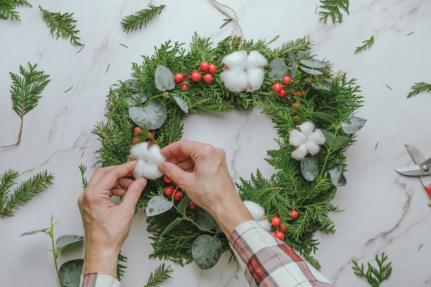 Making Christmas wreath with evergreen twigs cotton balls and holly berries