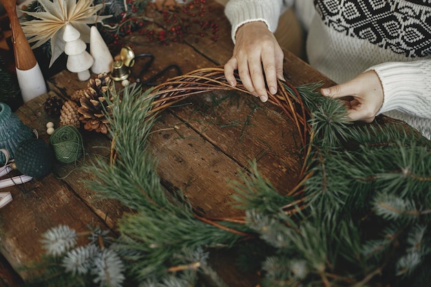 Photo making christmas wreath woman holding pine branches and arranging xmas wreath on rustic background