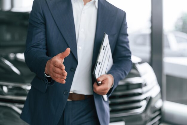 Photo making a deal giving a hand holding notepad a businessman is in a car dealership