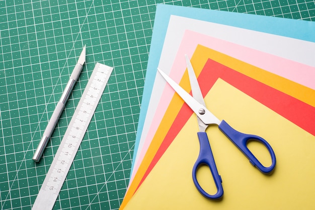 Making different models with paper. Artwork with papers. Scissors, scalpel, pile of papers and ruler on cutting mat