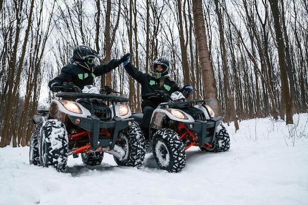 Photo making high five two people are riding atv in the winter forest