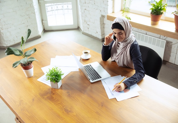 Making notes while talking on phone Arabian businesswoman wearing hijab while