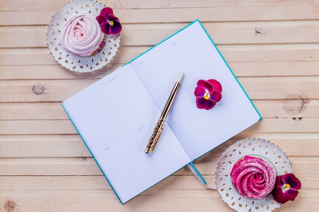 Making plans in tiny notebook for christmas.decorations and sweet pink marshmallows.Colorful zephyr on wooden wall.weekly planner or to do list with pen. planning holidays concept