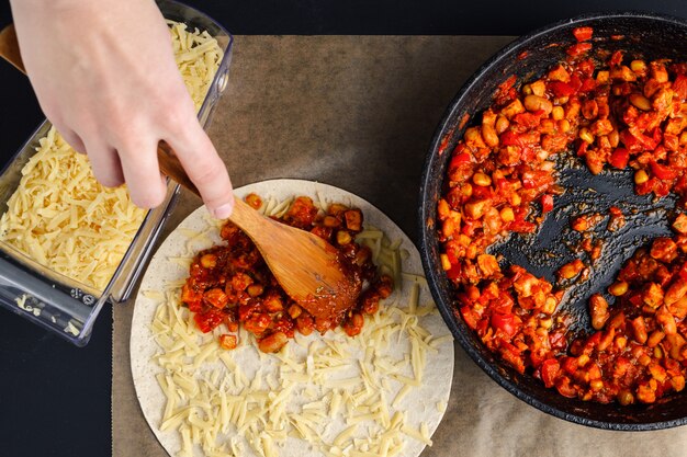 Photo making of quesadilla, a woman spreads a stuffing from a frying pan on a tortilla