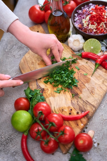 Making salsa dip sauce woman cutting and chopping cilantro or parsley on wooden cutting board