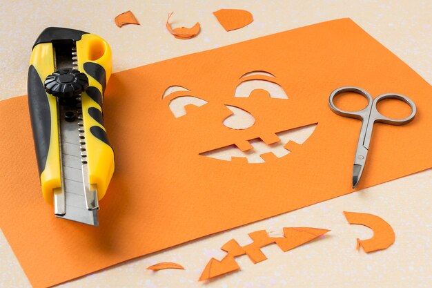 Making stencil of orange paper for jackolantern using stationery knife and scissors