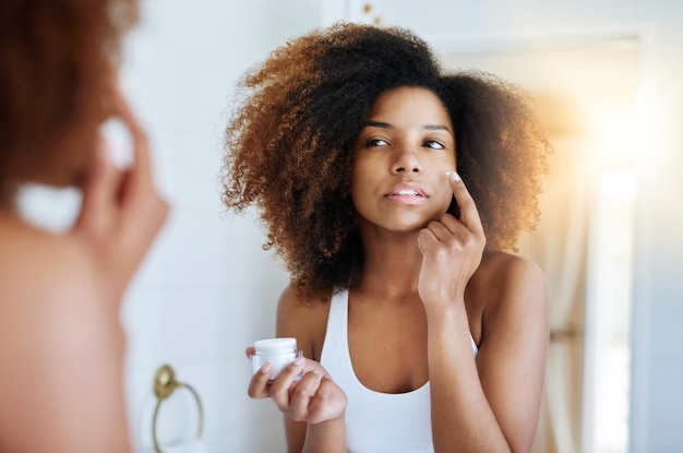 Making sure her skin stays hydrated all day Shot of an attractive young woman applying moisturizer to her face in front of the mirror