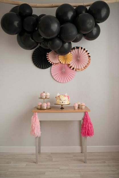 Making a sweet table for a birthday. Cake cat and garland of black balls. Pink and black design.