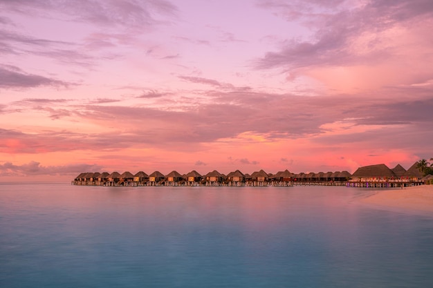 Maldives island, luxury water villas resort and wooden pier. Beautiful sky and clouds and beach