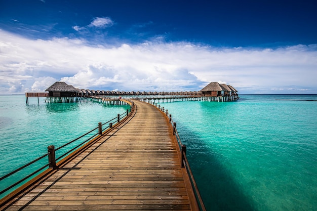 Maldives island, luxury water villas resort and wooden pier. Beautiful sky and ocean lagoon beach