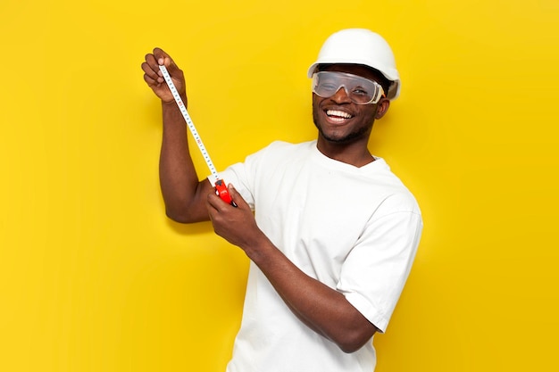 male african american builder in uniform holds tape measure on yellow isolated background