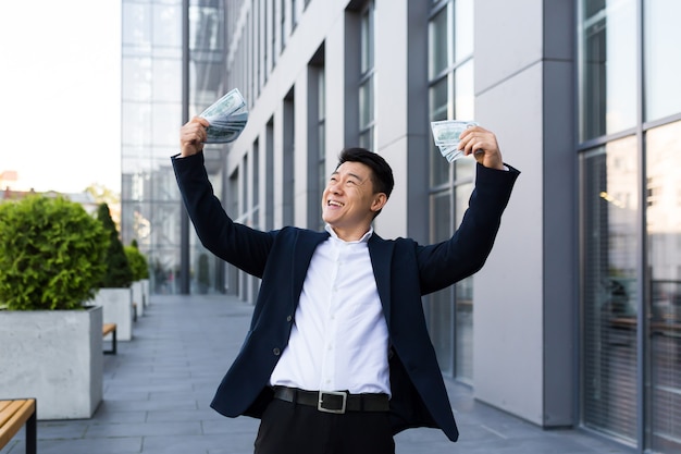 Male asian businessman rejoices holding a lot of cash dollars got a big win and payout