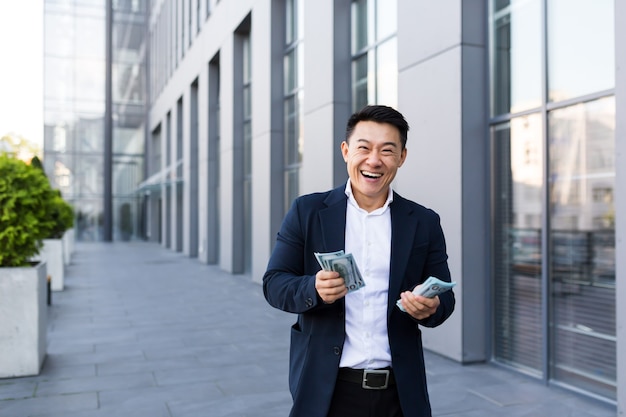 Male asian businessman rejoices holding a lot of cash looking at the camera giving money