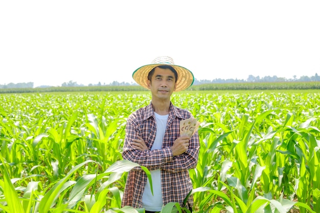 A male Asian farmer in a striped shirt wearing a hat posing standing with the corn income bills