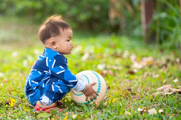 A male Asian kid holding and playing with a football in the outdoor backyard