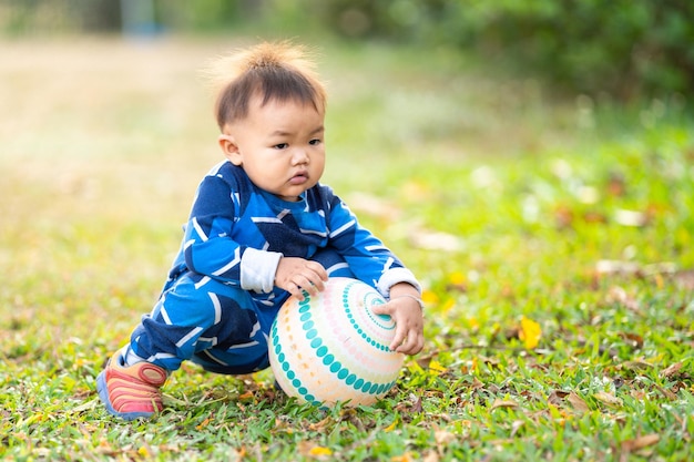 A male Asian kid holding and playing with a football in the outdoor backyard