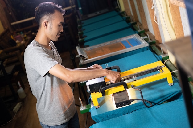 Male Asian workers carefully hold the heater to dry the screen printing ink after printing