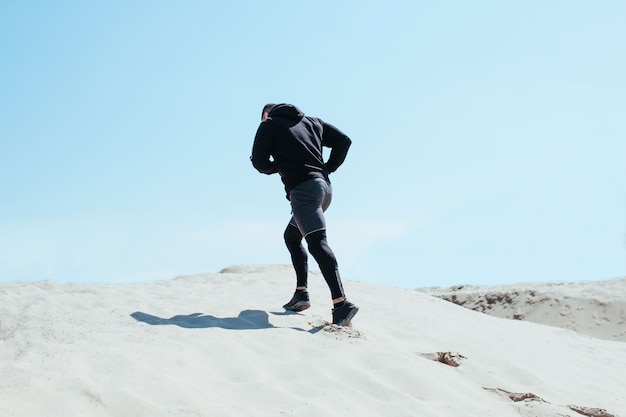 Male athlete runs on a sandy mountain