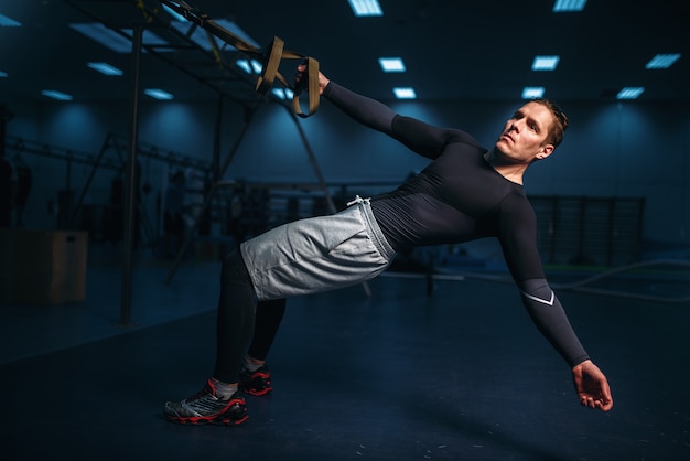 Male athlete on training, stretch workout with ropes in gym.