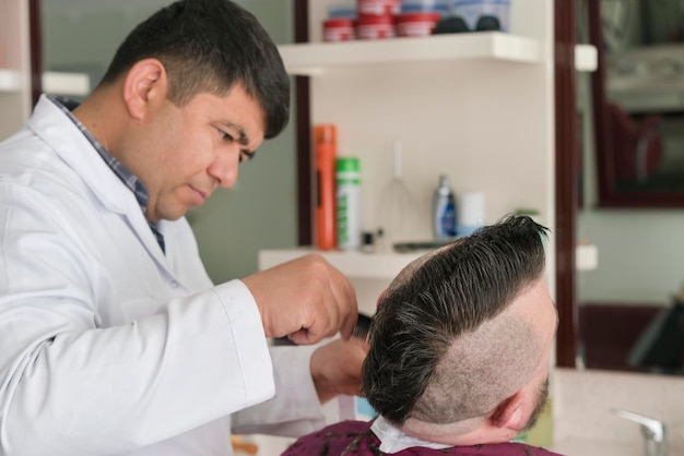 Male barber cuts the beard of a adult man with a mohawk