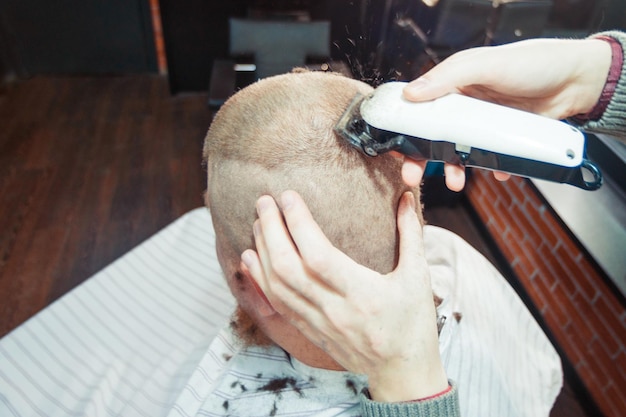 A male barber is cutting hair with trimming machine