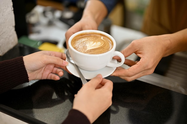 A male barista handing a cup of latte to a customer in the coffee shop