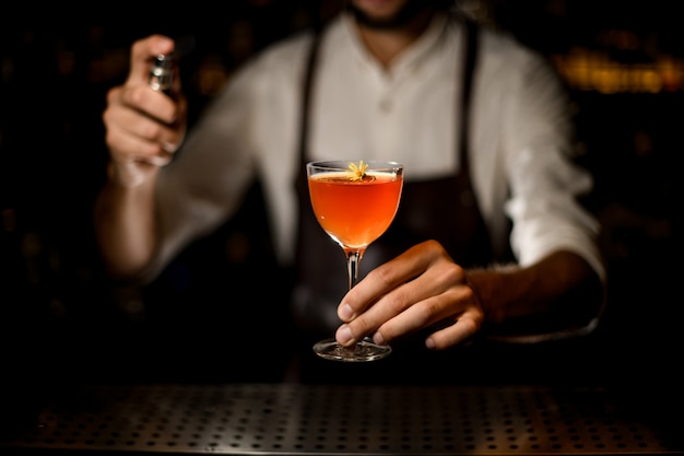 Male bartender serving a cocktail in the glass  spraying on it