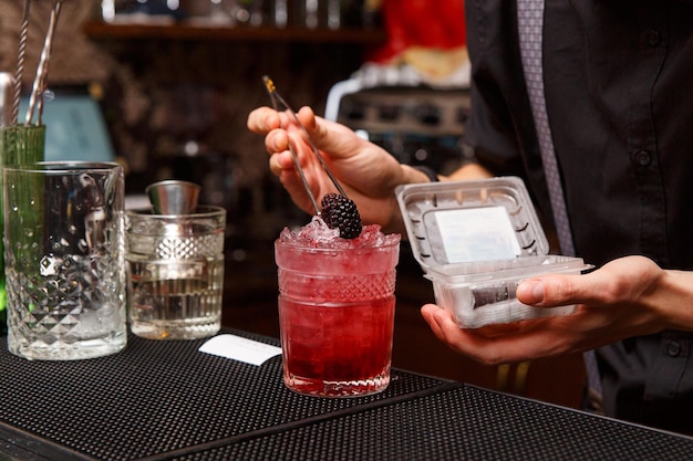 A male bartender uses tweezers to carefully decorate the finished cocktail