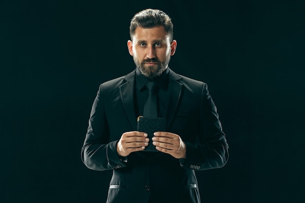 Male beauty concept portrait of a fashionable young man with stylish haircut wearing trendy suit posing over black wall