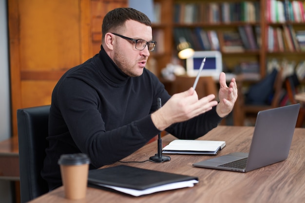 Male blogger streaming from library using laptop and microphone