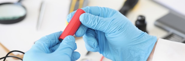 Male in blue gloves holding red battery piece repairing broken or damaged device by himself