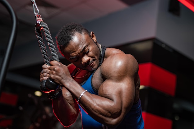 Male bodybuilder in dark sport wear doing workout for hands in modern gym Handsome athlete with perfect strong body