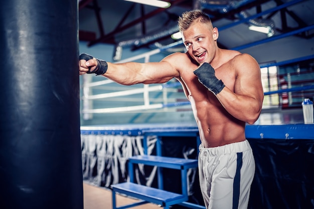 Male boxer training with punching bag in dark sports hall.