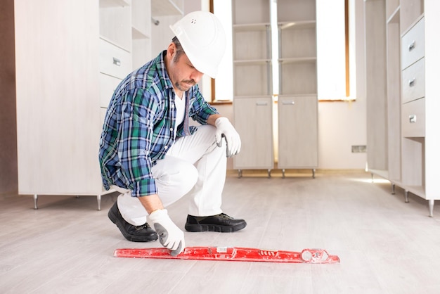 A male builder checks the evenness of the floor with a building level