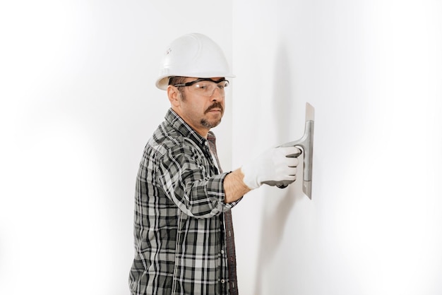 Male builder in a hard hat plastering a white wall