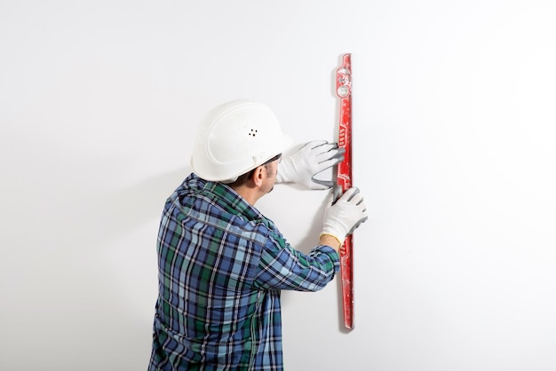 A male builder in a helmet checks a smooth wall with a building level