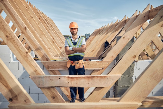 Male builder looking contented and wearing full uniform and gear while having his arms crossed on chest