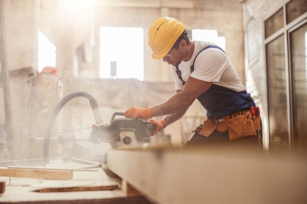 Male builder using wood cutting circular saw machine in workshop